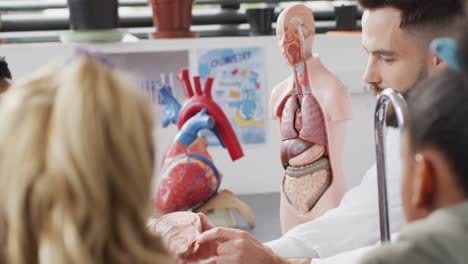 maestro masculino diverso y escolares felices estudiando el modelo del cuerpo humano en la clase de biología