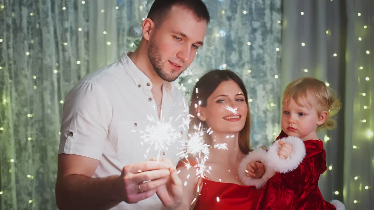 Parents and daughter wearing elegant clothes are holding sparklers, celebrating Christmas or New Year's Eve together in a festively decorated home