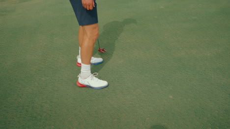 slow-motion clip showing a male golfer from the waist down walking across the putting green with a red putter, to read the green. capturing calm preparation, rhythm, and detail ahead of a putt.