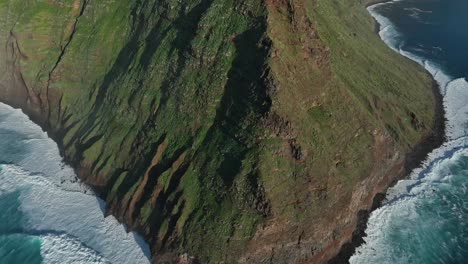 las fuertes olas del océano se estrellan en la base del acantilado de ponta vigia, el dron se inclina hacia el faro de ponta do pargo, portugal