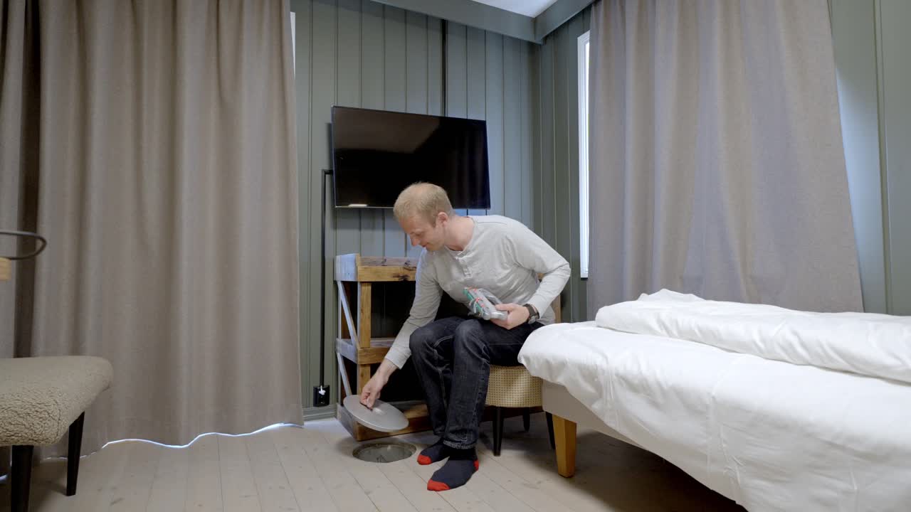 Man opens floor hatch and prepares fishing gear inside unique Lofoten hotel room