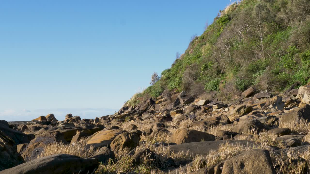 Slow motion landscape of rocky boulder formations along hiking trail surrounded by trees in bushland forest on a coastal headland within a national park Bateau Bay Central Coast Australia nature
