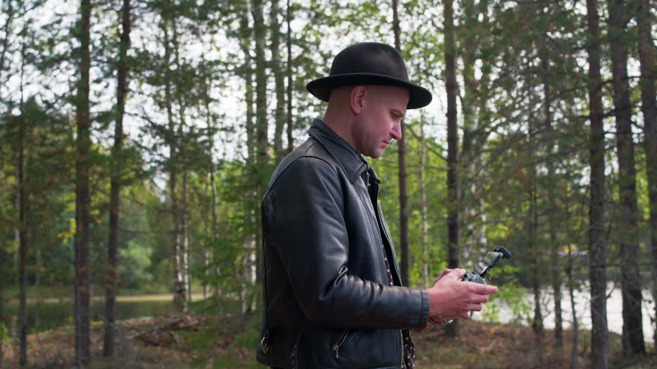 Caucasian model operating a drone in the forest and looking to his device