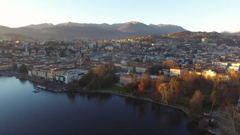 a drone view of a beautiful town surrounded by mountains, next to a lake, during a sunset in autumn