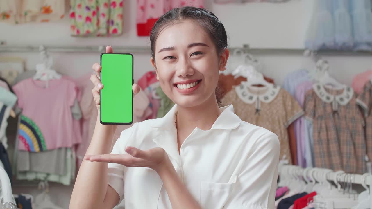 부티크에서 쇼핑하는 동안 카메라에 녹색 화면 스마트폰 모형을 보여주고 미소 짓는 아시아 어머니의 클로즈업
