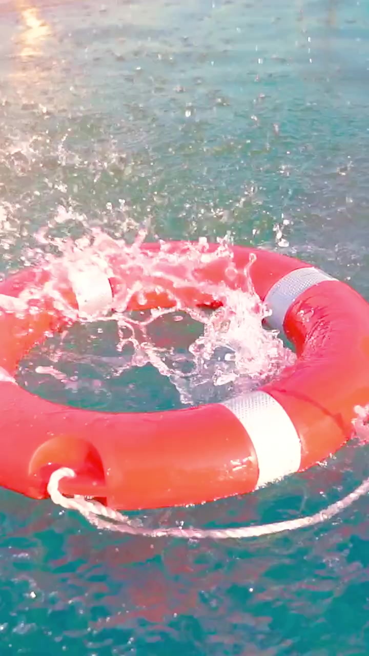 A vibrant orange lifebuoy tumbles into the refreshing turquoise ocean, creating ripples as it meets the water’s surface. The warm afternoon light enhances the charming scene.