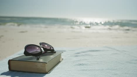 Nahaufnahme-Von-Buch,-Sonnenbrille-Und-Handtuch-Am-Strand,-In-Zeitlupe,-Mit-Kopierraum