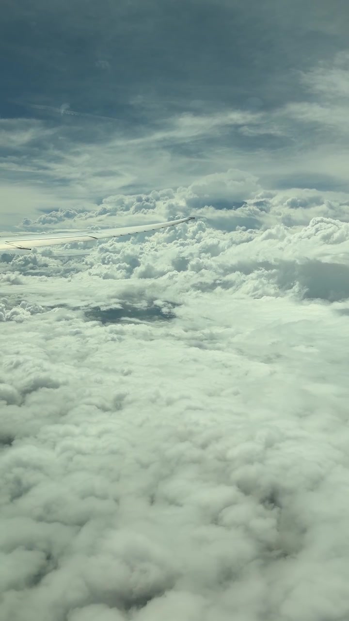 Aircraft flying above dreamy clouds. Window seat passenger point of view. Airplane wing tip.