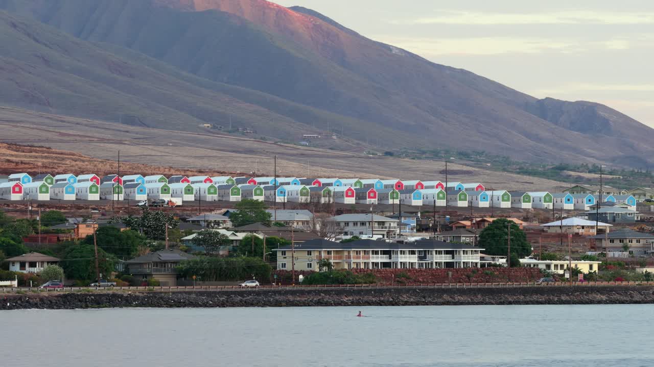 Bir drone, Lahaina, Maui'deki renkli modüler konutları görüntülüyor. Batı Maui Dağları, 2023'teki yıkıcı yangınlardan sonraki manzarayı göstererek arka planda yükseliyor