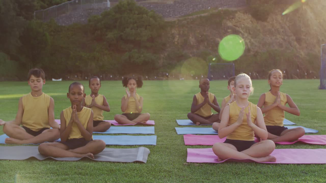 grupo diverso de escolares sentados en esteras meditando durante una lección de yoga al aire libre