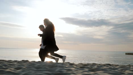 una pareja joven corriendo en la playa de arena. una pareja divirtiéndose, engañándose, tomándose de la mano, disfrutando del momento. una puesta de sol romántica durante las vacaciones de primavera, las vacaciones de luna de miel. una chica juguetona y un hombre enamorado.