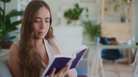 mujer centrada en leer un libro mientras está sentada en el sofá en casa