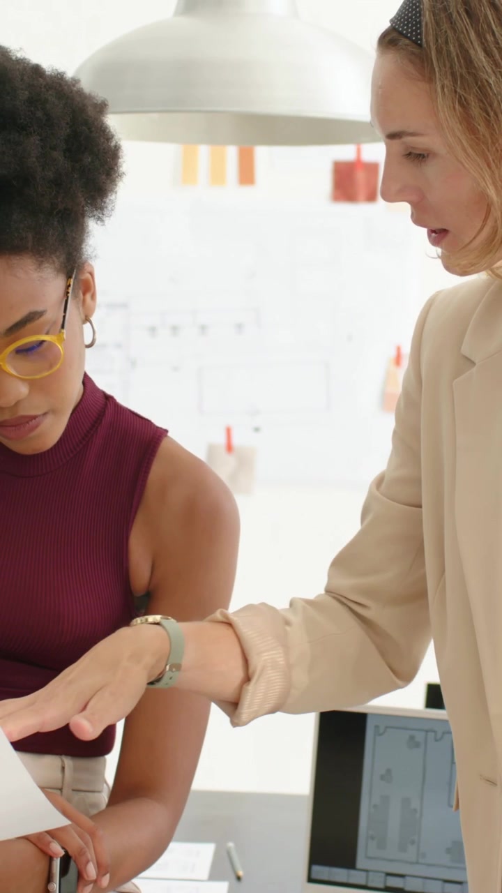 Vídeo vertical: Mulher sorrindo de blazer inclinada na mesa, explicando laptop e papéis, com espaço para texto