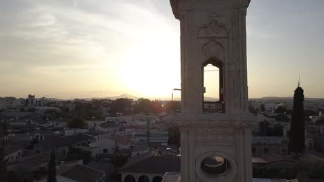 Toma-Aérea-Rodeando-La-Torre-De-Una-Iglesia-Con-Campanas-De-Iglesia-Sonando-Al-Atardecer