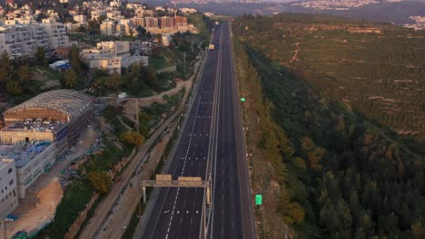 aerial view of an empty highway between a residential area and forested hills at dawn or dusk