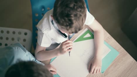 High-angle-shot-Children-boys-do-school-homework-sitting-at-a-table-in-a-notebook-thinking