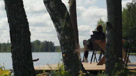 View-of-woman-through-the-trees-relaxing-on-a-deck-overlooking-a-lake-on-vacation