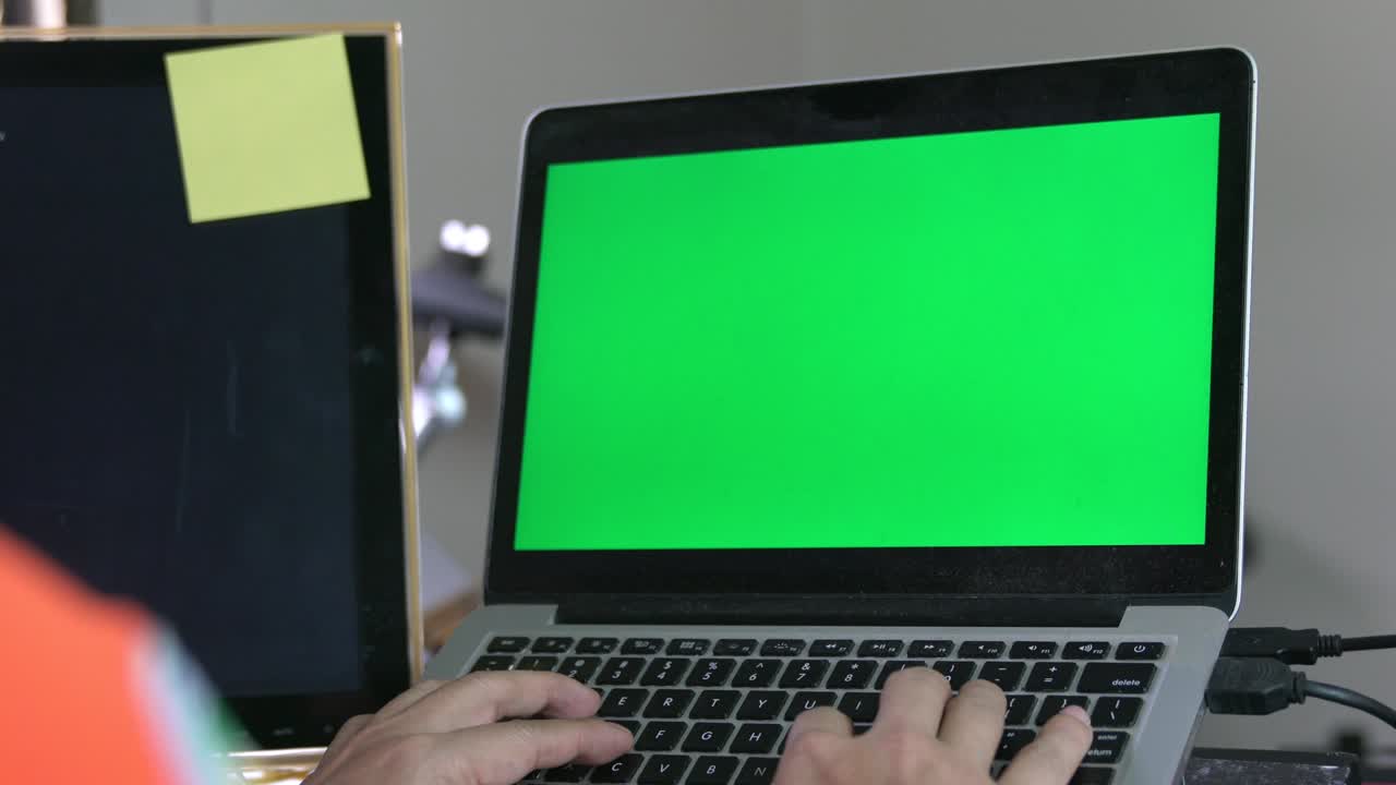 Man working at home on computer laptop, looking at green screen.
