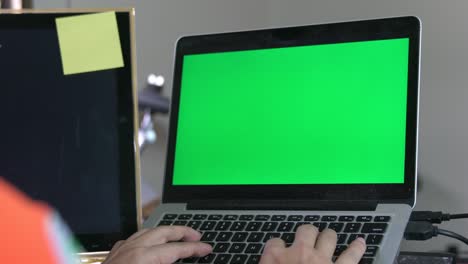 man working at home on computer laptop, looking at green screen.