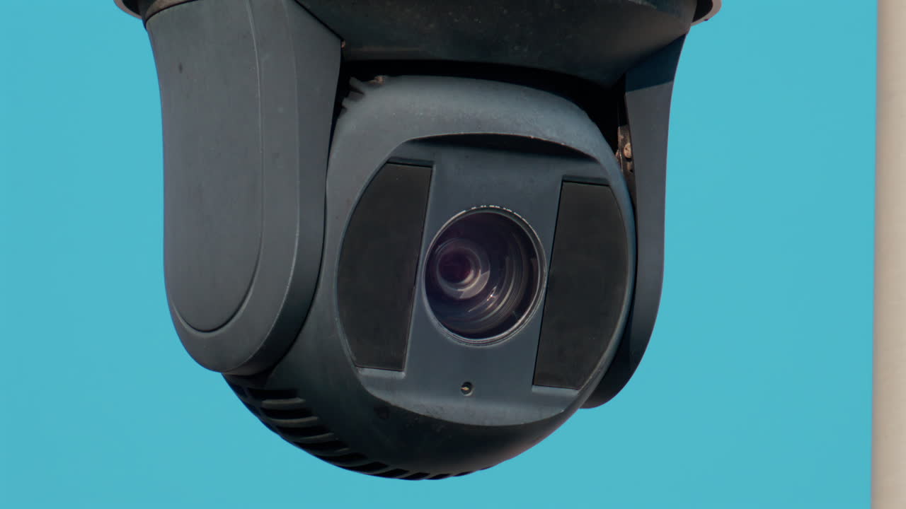 A close up of a modern black surveillance camera turning against a bright sky background