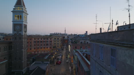 Vuelo-Nocturno-Por-Encima-De-La-Calle-En-El-Centro-De-La-Ciudad-Al-Atardecer.-Vuela-Alrededor-De-La-Antigua-Torre-Cuadrada-Con-Relojes-De-Torre.-Roma,-Italia