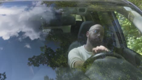 Bearded-man-drives-on-a-bumpy-dirt-road-through-a-thickly-wooded-area