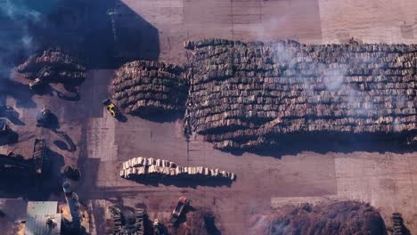 smoke above stack of logs in open storage area at sawmill industry