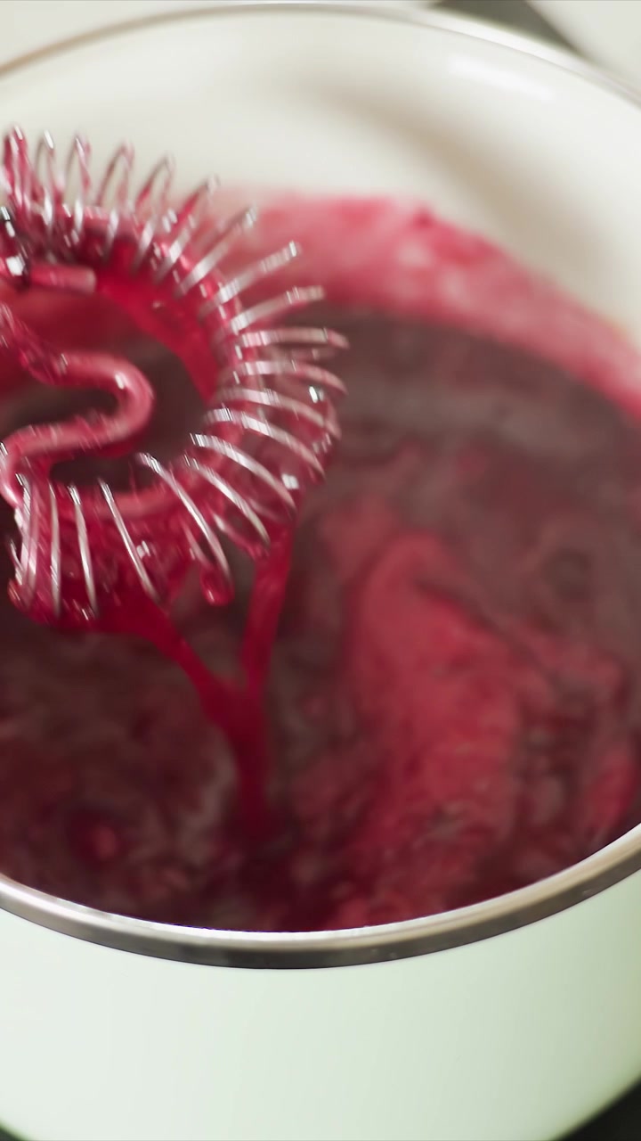 Close up of thick dark red liquid being stirred in white pot. Mixture bubbles and changes texture as it is continuously mixed. Steady view captures rich color with stirring