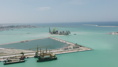 wide aerial footage of construction ships in the harbor building new land in the water