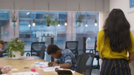 Woman-Walking-Into-An-Office-And-Sitting-Down-With-Colleagues