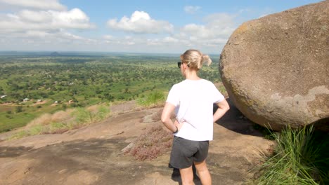 Toma-En-Cámara-Lenta-Orbitando-Alrededor-De-Una-Excursionista-Occidental-Rubia-Mientras-Se-Para-En-La-Cima-De-Una-Montaña-En-El-Este-De-África-Mirando-Las-Vistas-Del-Paisaje