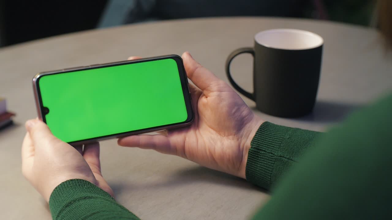 Donna che usa uno smartphone con schermo verde in modalità orizzontale. Guarda contenuti, video, blog e preme il pulsante play sullo schermo verde (chroma key).