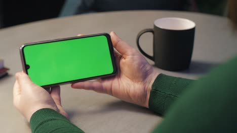 woman using smartphone with green screen in horizontal landscape mode. girl using mobile phone, watching content, videos, blogs. woman pressing play button on the green screen, chroma key
