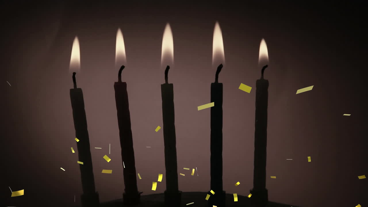 Coriandoli dorati che cadono sopra la silhouette di diverse candele accese su sfondo grigio.