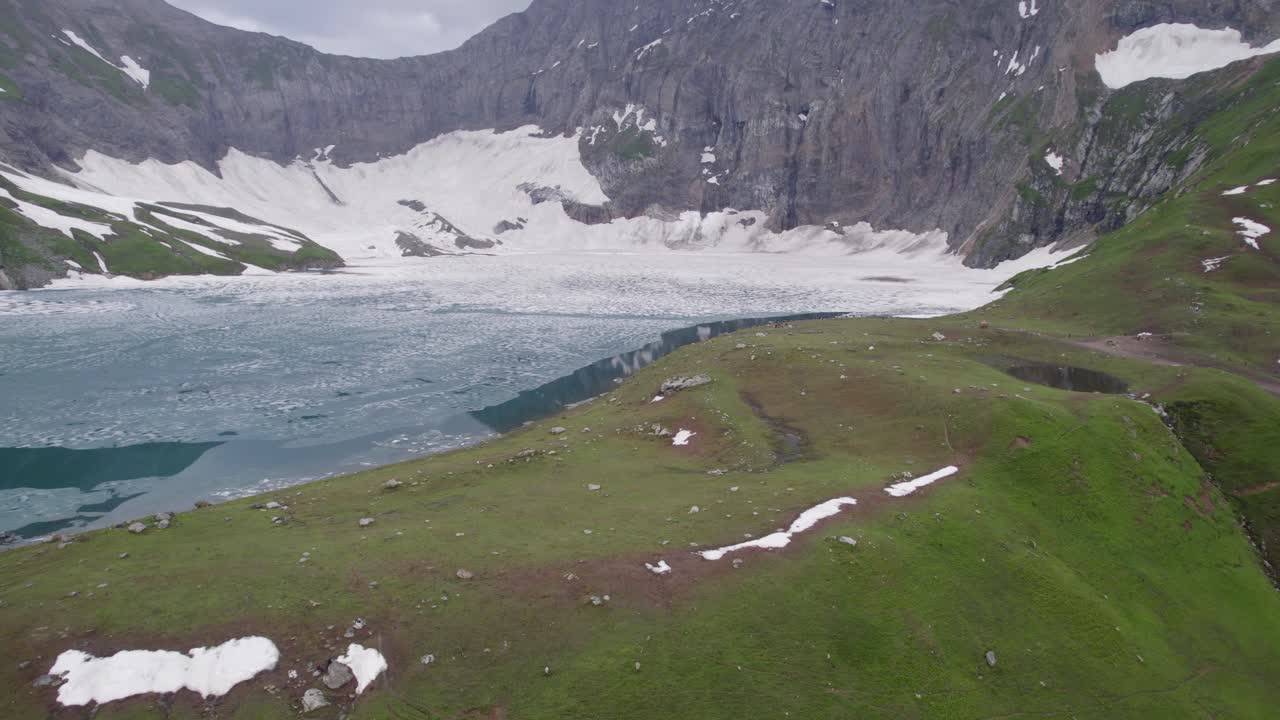 lago alpino parcialmente congelado con laderas cubiertas de nieve y montañas escarpadas en el fondo