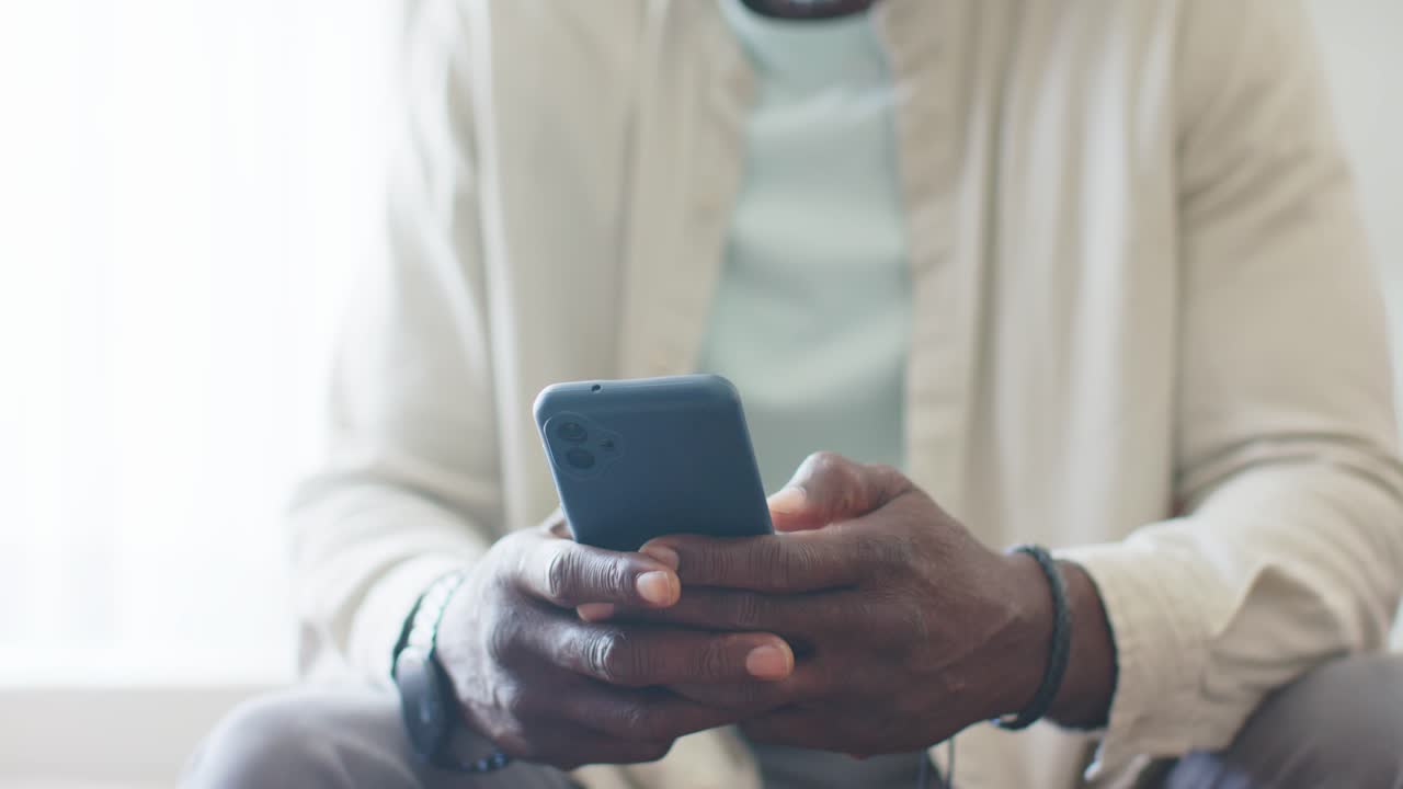 African American mature man tapping blue smartphone, camera pulling back revealing smile by window