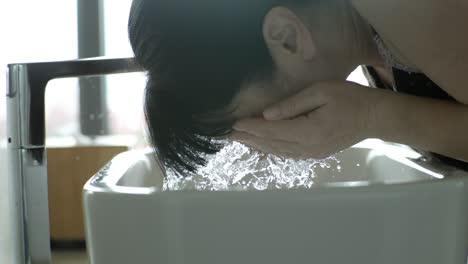 una mujer lavándose la cara con agua en el fregadero del baño a cámara lenta. filmado con una cámara súper a cámara lenta de 1000 fps.