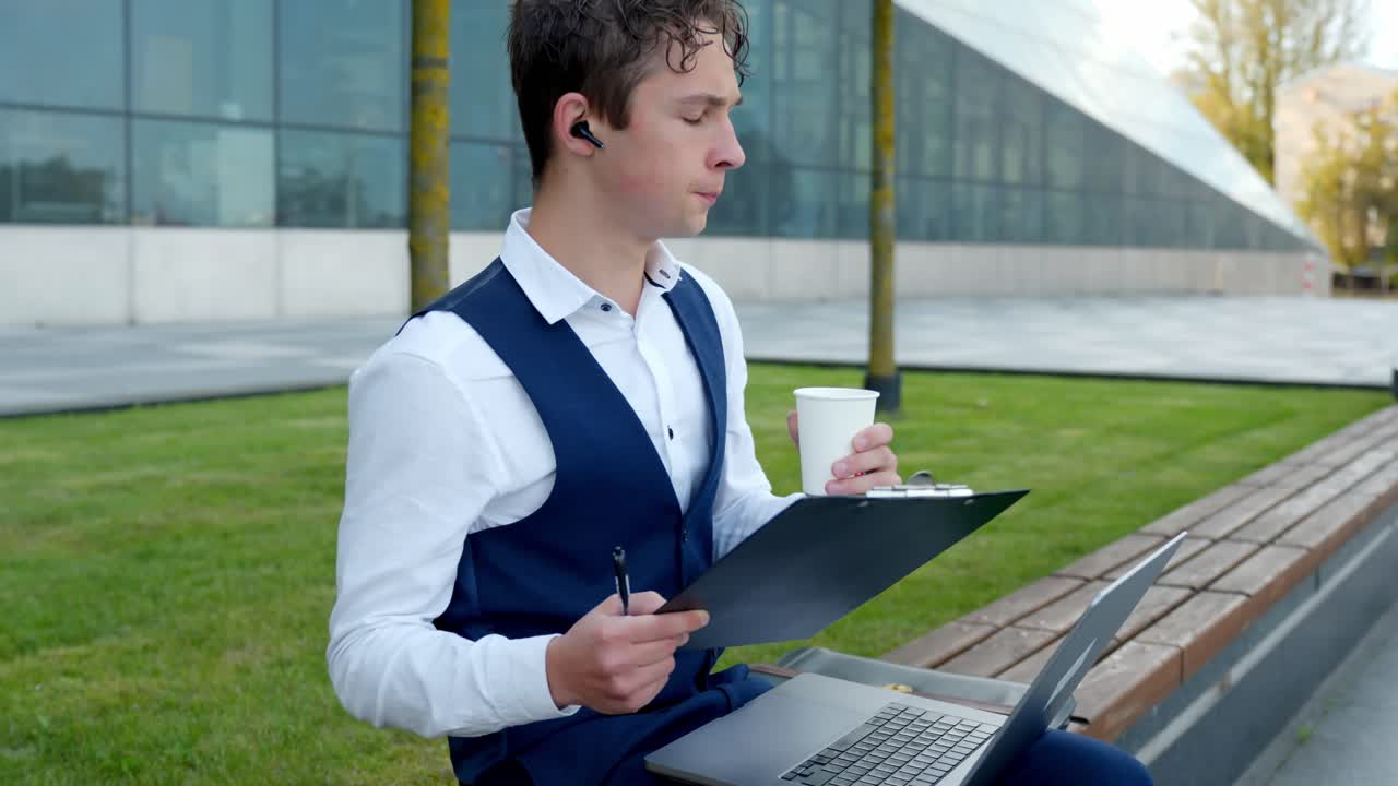 Young finance analyst working on laptop and drinking coffee outside office