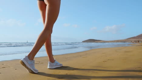 close-up of leg sporty woman in white sneakers running along beautiful sandy beach, healthy lifestyle in slow motion