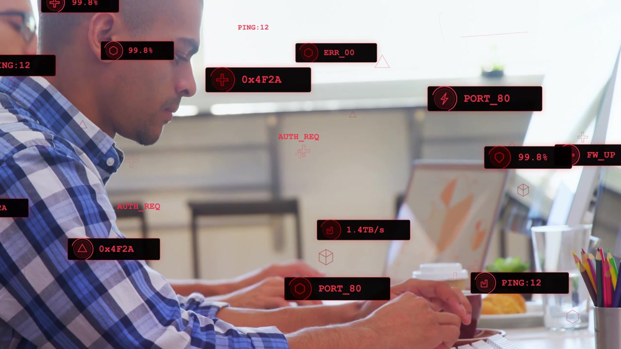 Foreground man typing and noting at shared desk, keystrokes activating HUD analyzing network data