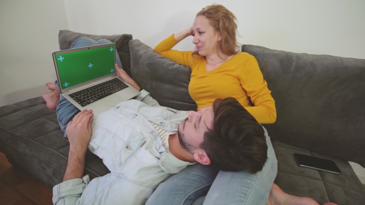 una pareja enamorada en un sofá mirando una computadora portátil. un niño tendido en el regazo de una niña. pantalla verde.