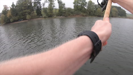 un pescador lanza un señuelo con su caña, está en un bote en un pequeño lago suizo