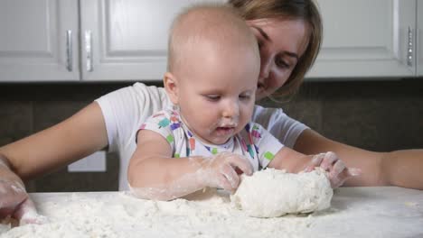 young mother and her little kid preparing dough on the table. little baby playing with flour. baker prepares the dough. family