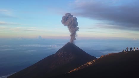 volcán en erupción al amanecer con gente parada en una colina mirándolo