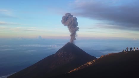 erupting volcano in the sunrise with people standing on a hill watching it