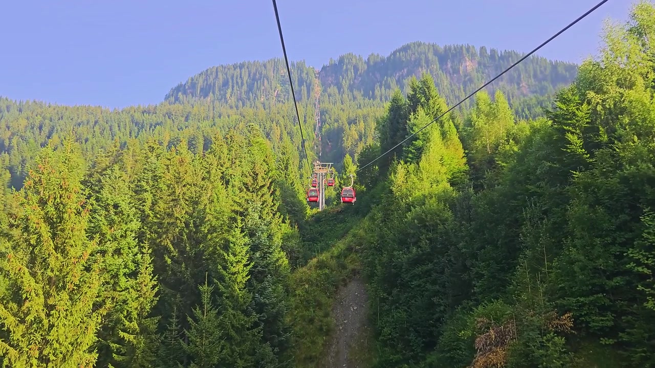 Kitzbühel, Austria, panorama alpino con cavi della funivia, tetti del villaggio turistico, campanili di chiese, valli verdi e montagne che brillano nella soffice luce del sole mattutino in uno scenario di viaggio estivo.