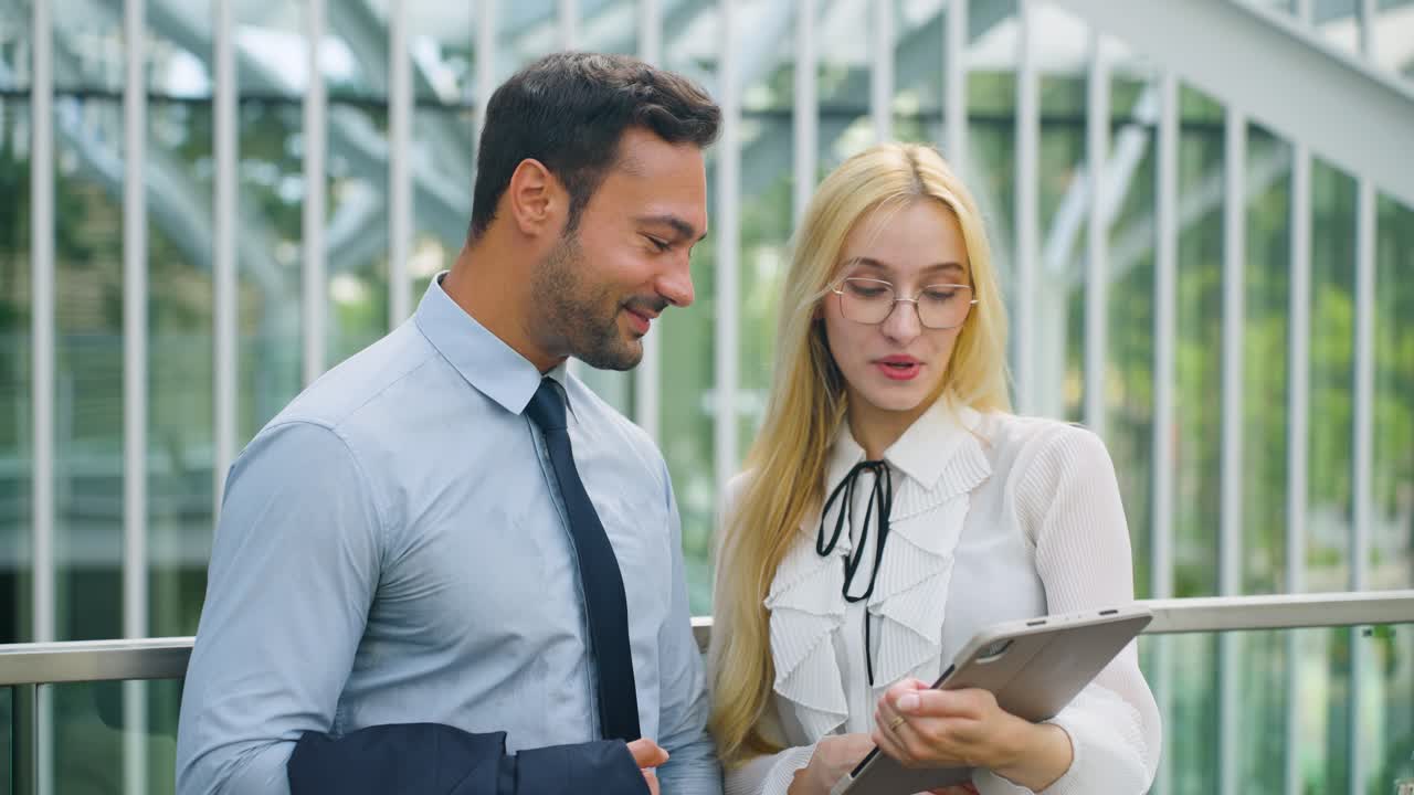 Two businesspeople are having a delightful discussion at outdoor city terrace, woman shows something on the tablet PC and they are both excited and smiling