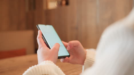 close up hand view of woman using smartphone in warm wooden cafe interior, fingers actively engaged with screen, showcasing technology interaction in calm setting with blurred
