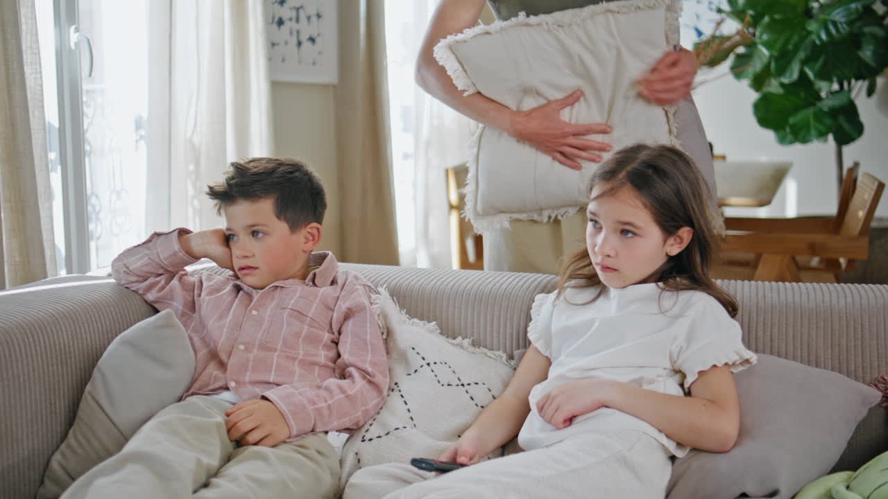 Caring mother kissing kids at cozy couch closeup. Two small children watching tv