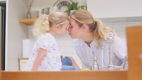 mother wearing rubber gloves at home in kitchen with young daughter having fun as they do washing up at sink- shot in slow motion